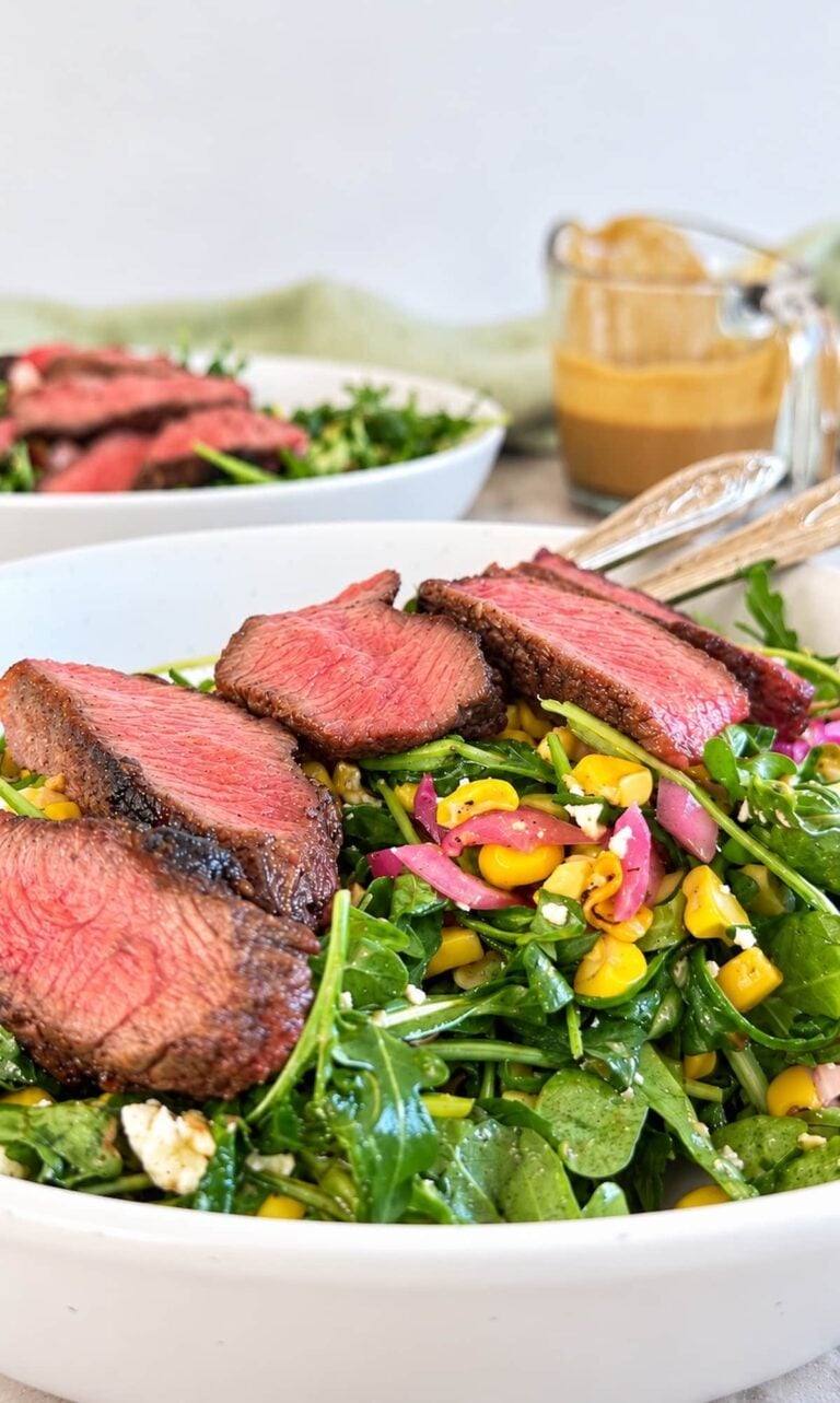 Arugula steak salad topped with juicy sliced steak, sweet corn, pickled red onions, crumbled cheese, and a creamy homemade dressing.
