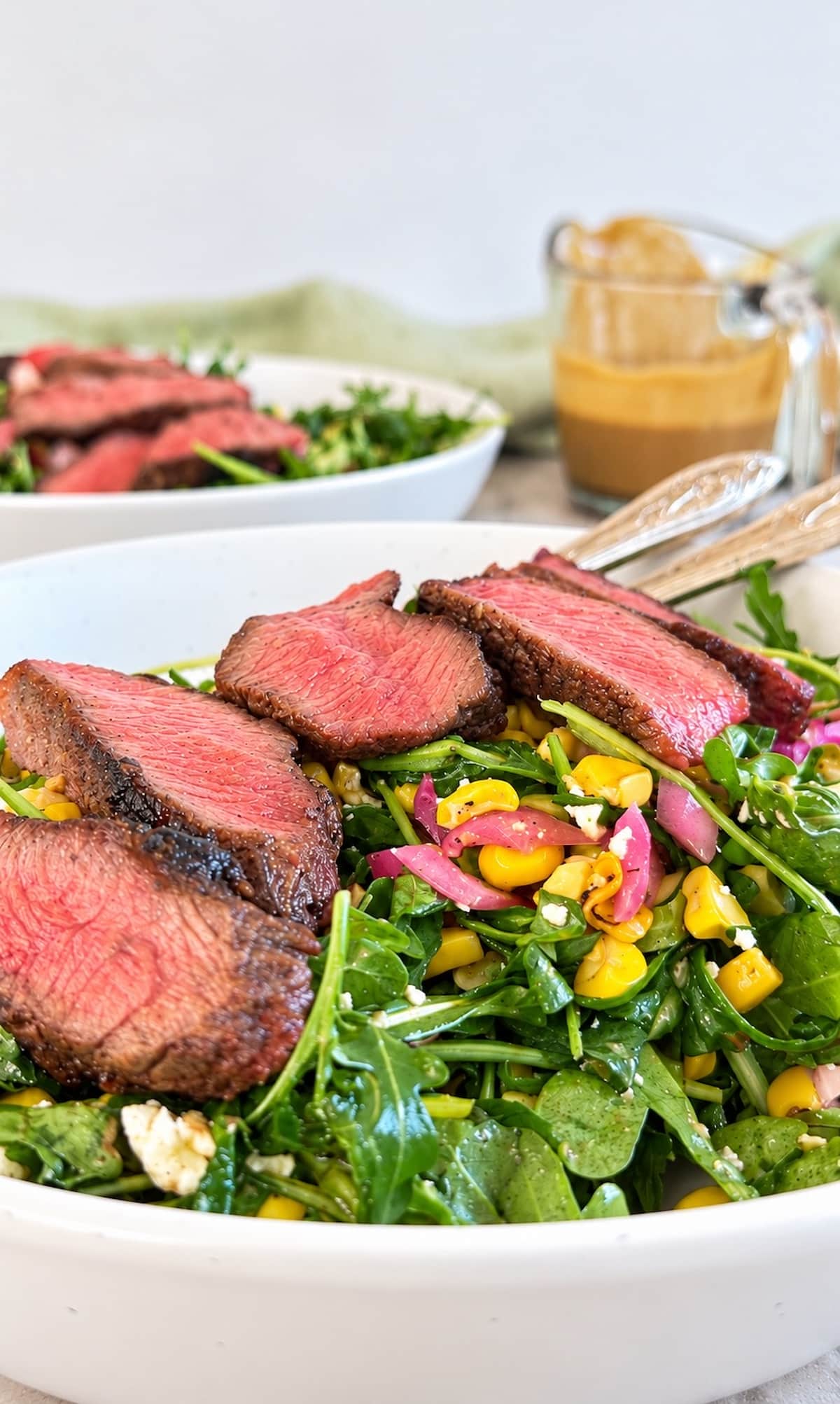 Arugula steak salad topped with juicy sliced steak, sweet corn, pickled red onions, crumbled cheese, and a creamy homemade dressing.