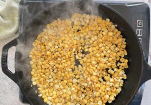 corn kernels cooking in a black cast iron skillet on a burner.