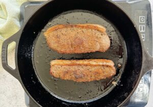 two seasoned cooked steaks in a black cast iron skillet on a burner.