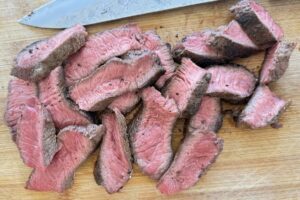 sliced medium rare steak on a cutting board with a knife.