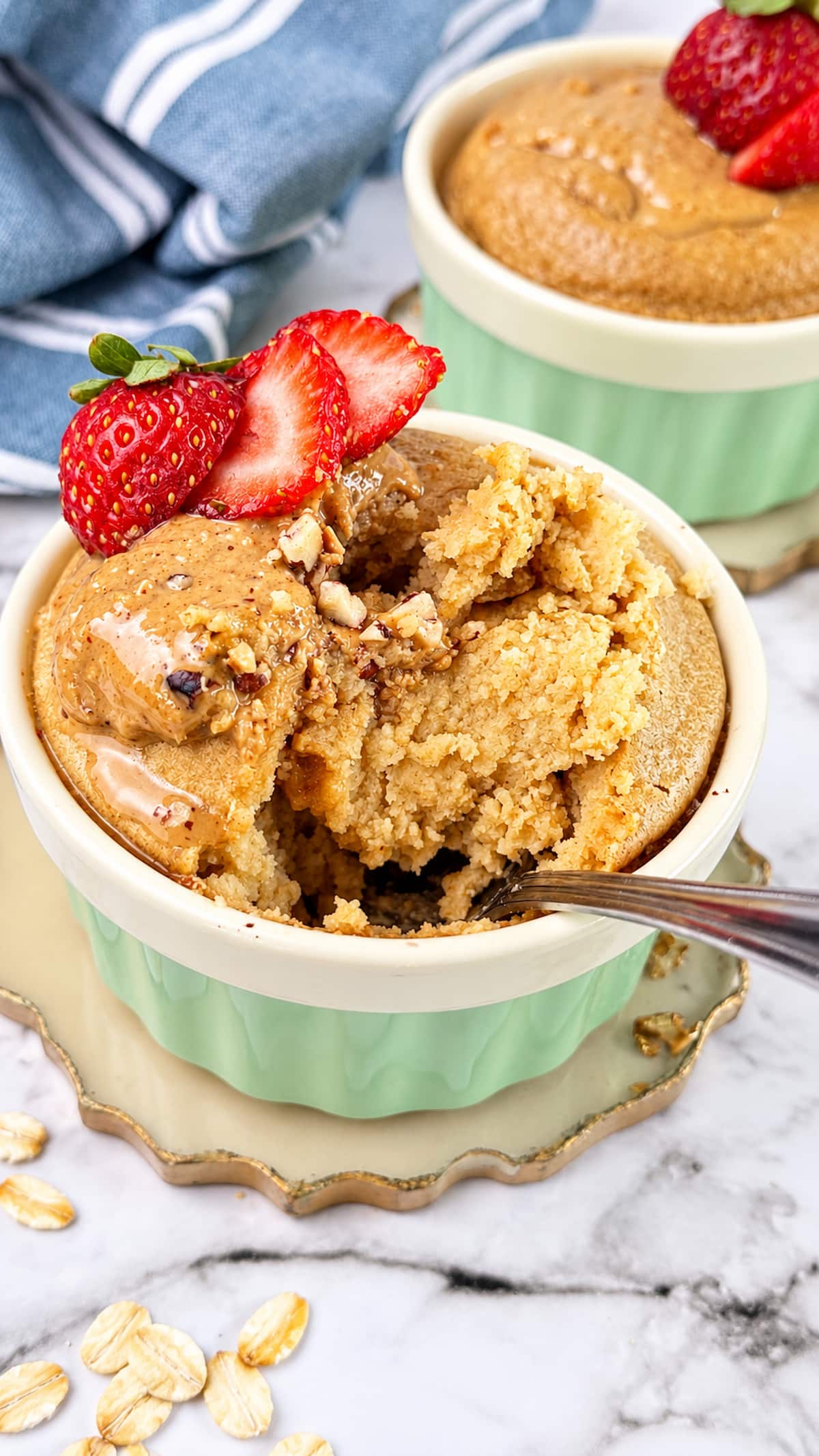 Baked oats without banana topped with creamy peanut butter, chopped nuts, and fresh strawberries, with a spoon revealing the soft, fluffy center.