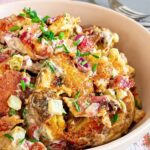 Smashed potato salad with crispy bacon, pickles, red onion, and fresh chives in a creamy dressing.