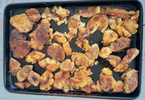 extra crispy smashed potatoes drizzled with olive oil and spices on a baking sheet.