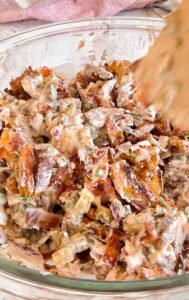 crispy smashed potato salad with bacon, red onions, pickles, chives, and creamy dressing in a large glass bowl.