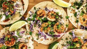 Jerk shrimp tacos with charred seasoned shrimp, creamy purple cabbage slaw, green onions, fresh cilantro, and lime wedges on warm flour tortillas.