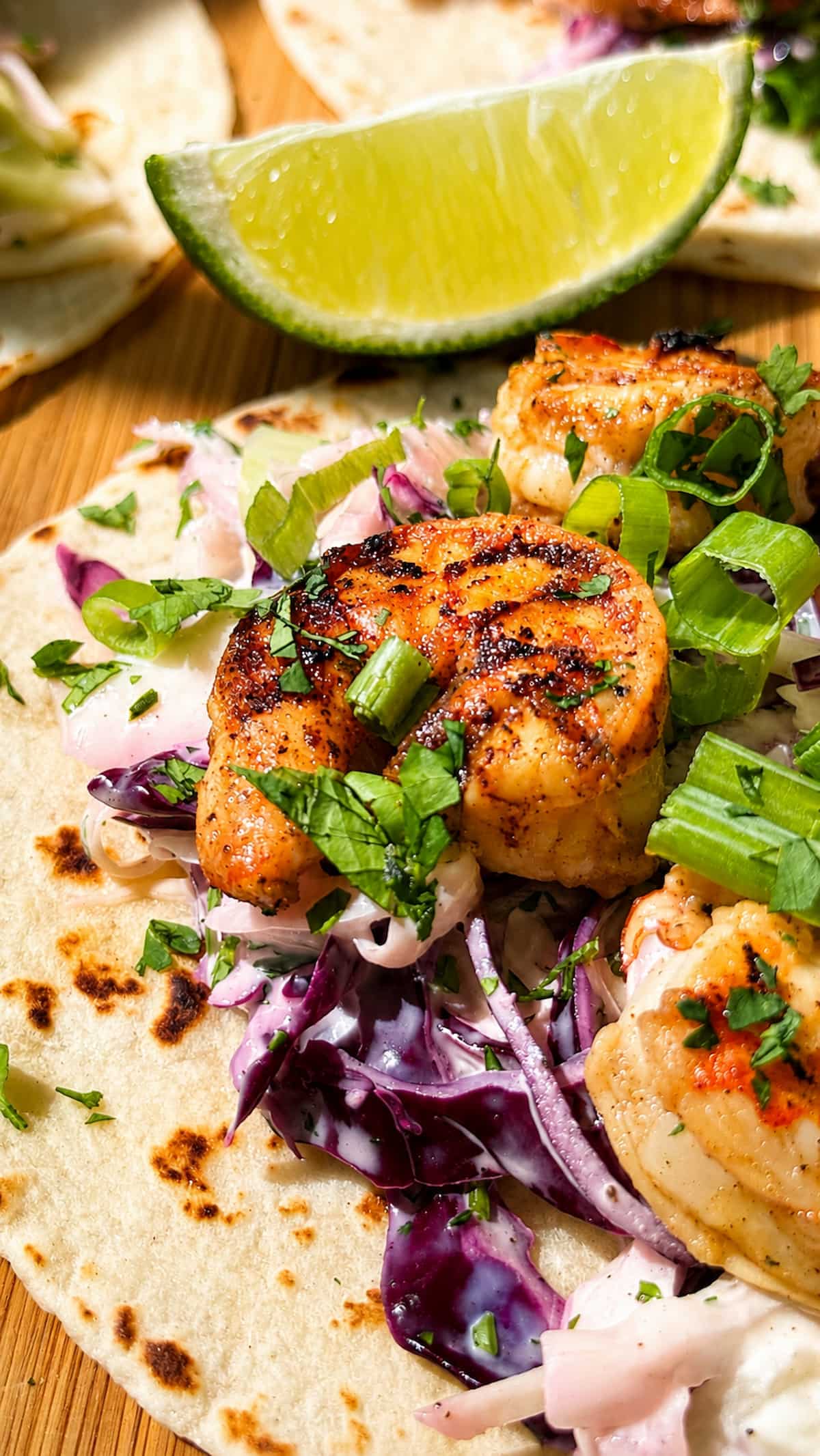 Jerk shrimp tacos with charred seasoned shrimp, creamy purple cabbage slaw, green onions, fresh cilantro, and a lime wedge on warm flour tortillas.