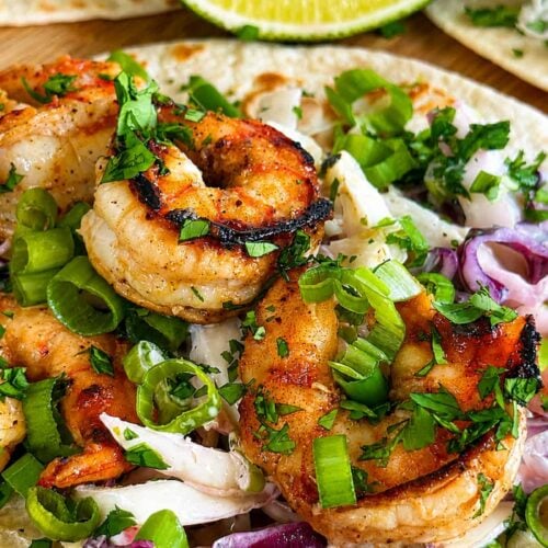Jerk shrimp tacos with creamy cabbage slaw, green onions, fresh cilantro, and lime.