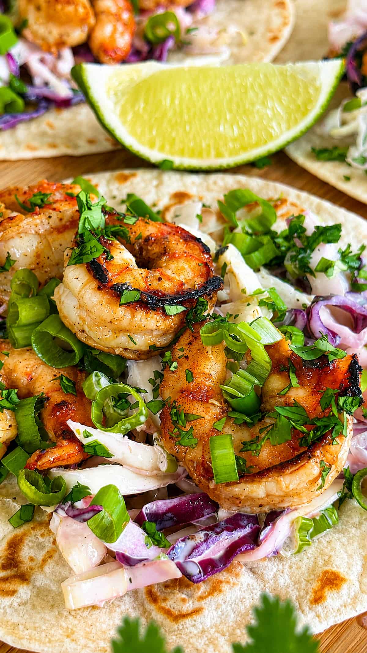Jerk shrimp tacos with creamy cabbage slaw, green onions, fresh cilantro, and lime.
