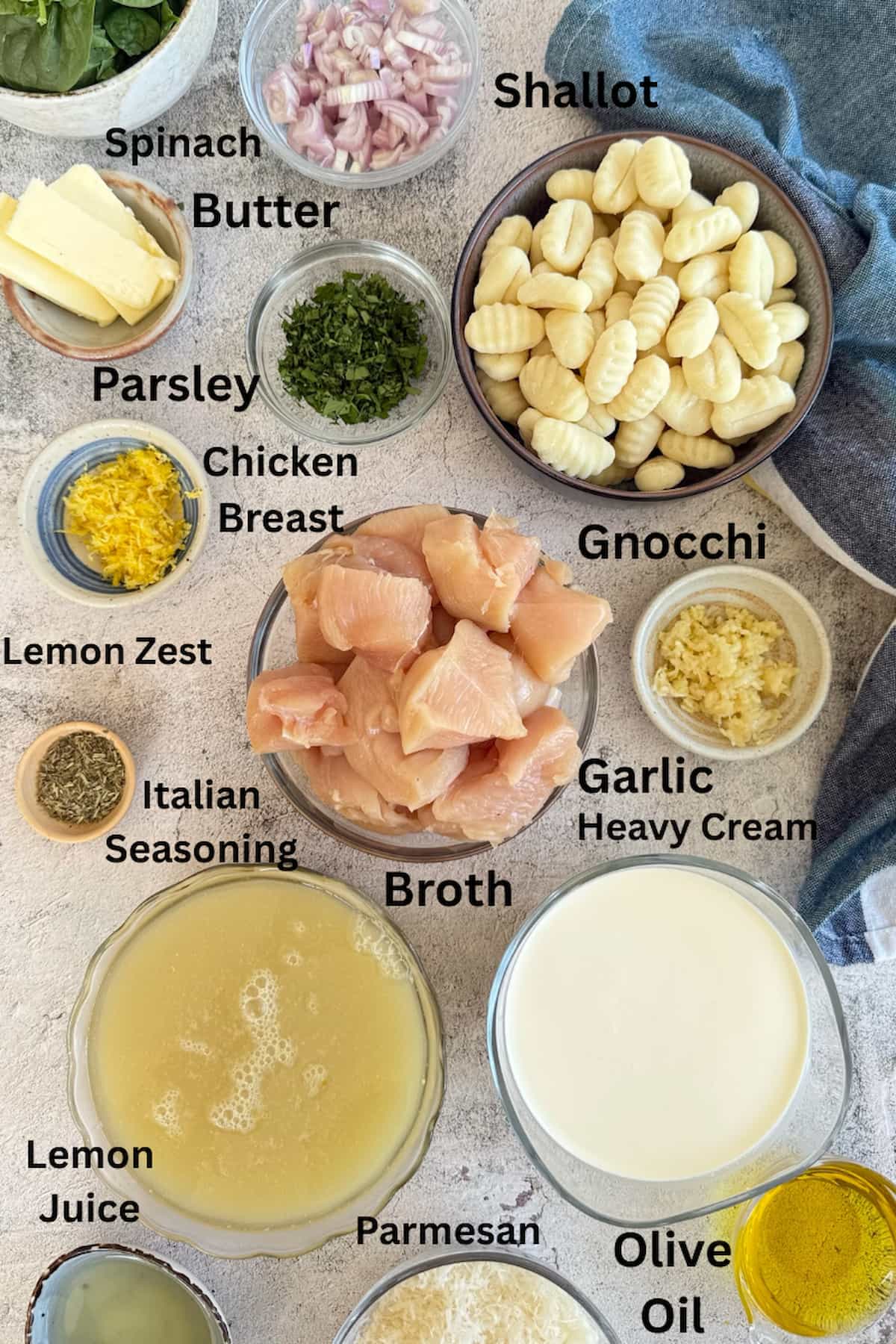 ingredients for lemon chicken gnocchi laid out in separate bowls - spinach, parsley, chicken breast, gnocchi, shallots, garlic, butter, lemon zest, lemon juice, broth, italian seasoning, salt, pepper, olive oil, parmesan, and heavy cream.