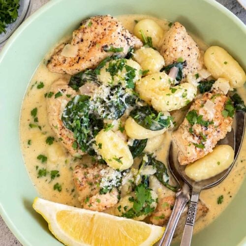 Creamy lemon chicken gnocchi with spinach, Parmesan, fresh parsley, and a lemon wedge.