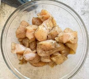raw seasoned chicken breast chunks in a glass bowl.
