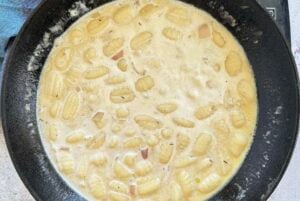 gnocchi cooking in a creamy white sauce in a cast iron skillet.