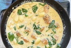 gnocchi with chicken chunks and spinach cooking in a creamy white sauce in a cast iron skillet.