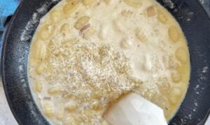 gnocchi cooking in a creamy sauce with parmesan on top, rubber spatula stirring it.