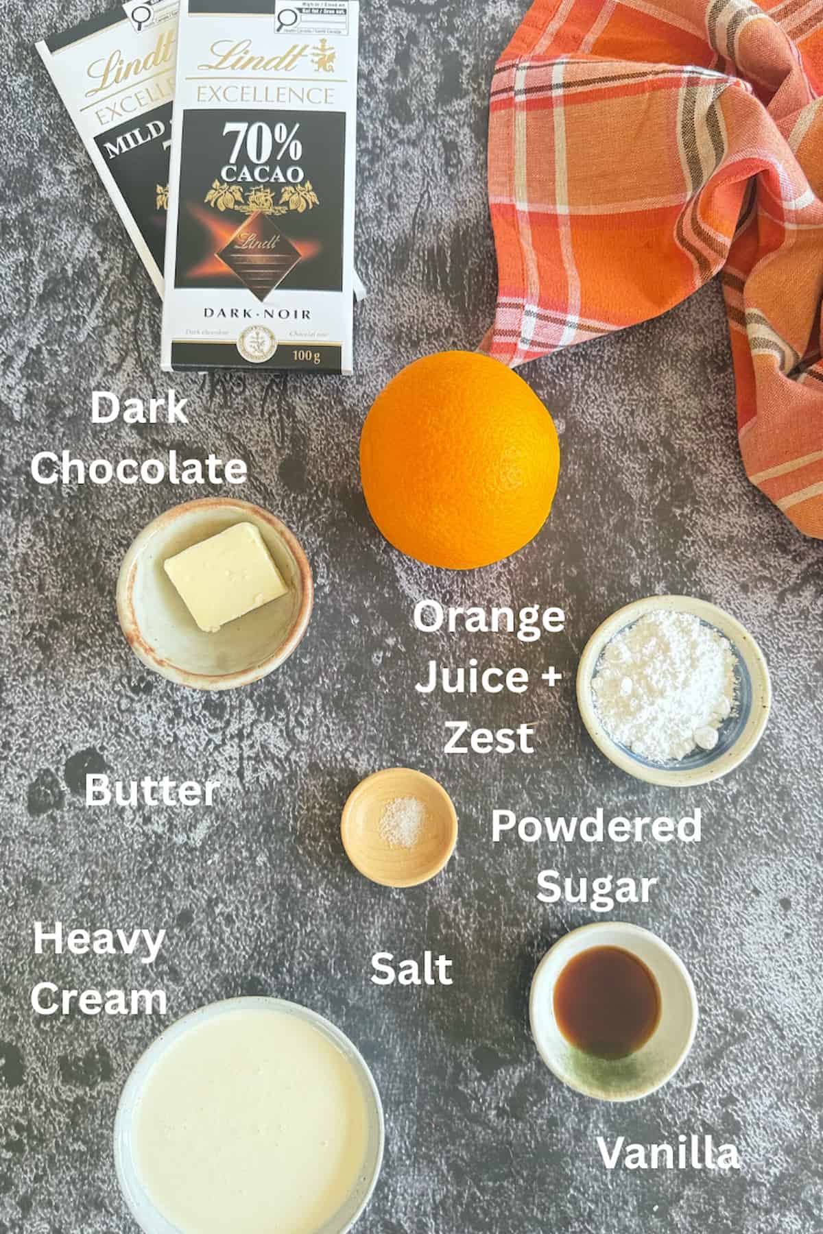 ingredients for orange and chocolate mousse laid out - 2 bars of dark chocolate, an orange, heavy cream, butter, powdered sugar, salt, and vanilla.