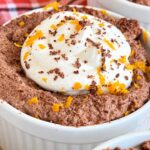 Chocolate orange mousse topped with whipped cream, orange zest, and chocolate shavings in a white ramekin.
