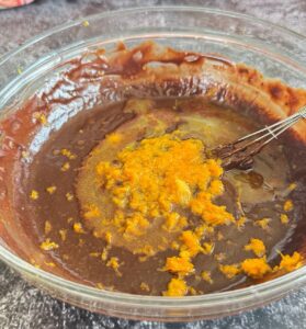 orange juice and zest on top of chocolate pudding in a bowl with a little whisk.