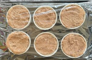 6 large ramekins filled with chocolate mousse on a baking sheet covered with plastic wrap.