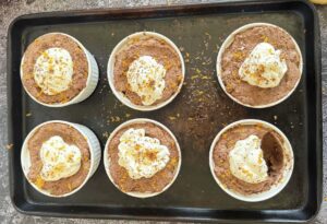sheet pan with 6 ramekins with orange chocolate mousse topped with whipped cream and orange zest, bite taken out of one.