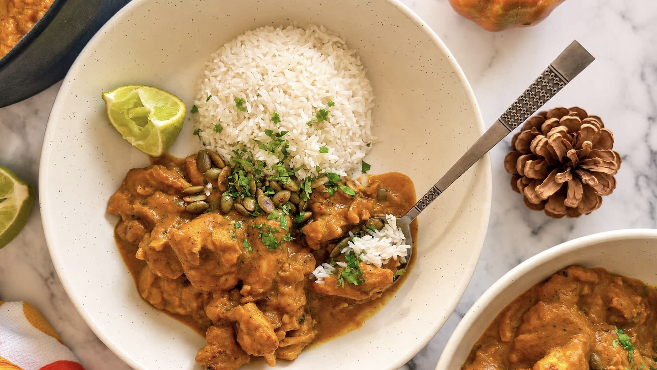 Pumpkin chicken curry with white rice, fresh cilantro, pumpkin seeds, and a lime wedge.