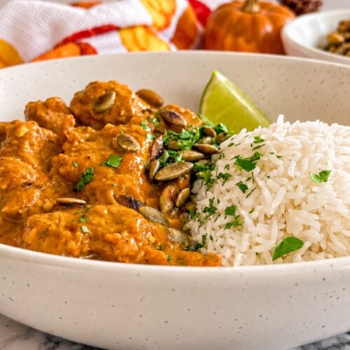 Pumpkin chicken curry with fluffy white rice, fresh cilantro, pumpkin seeds, and a lime wedge.