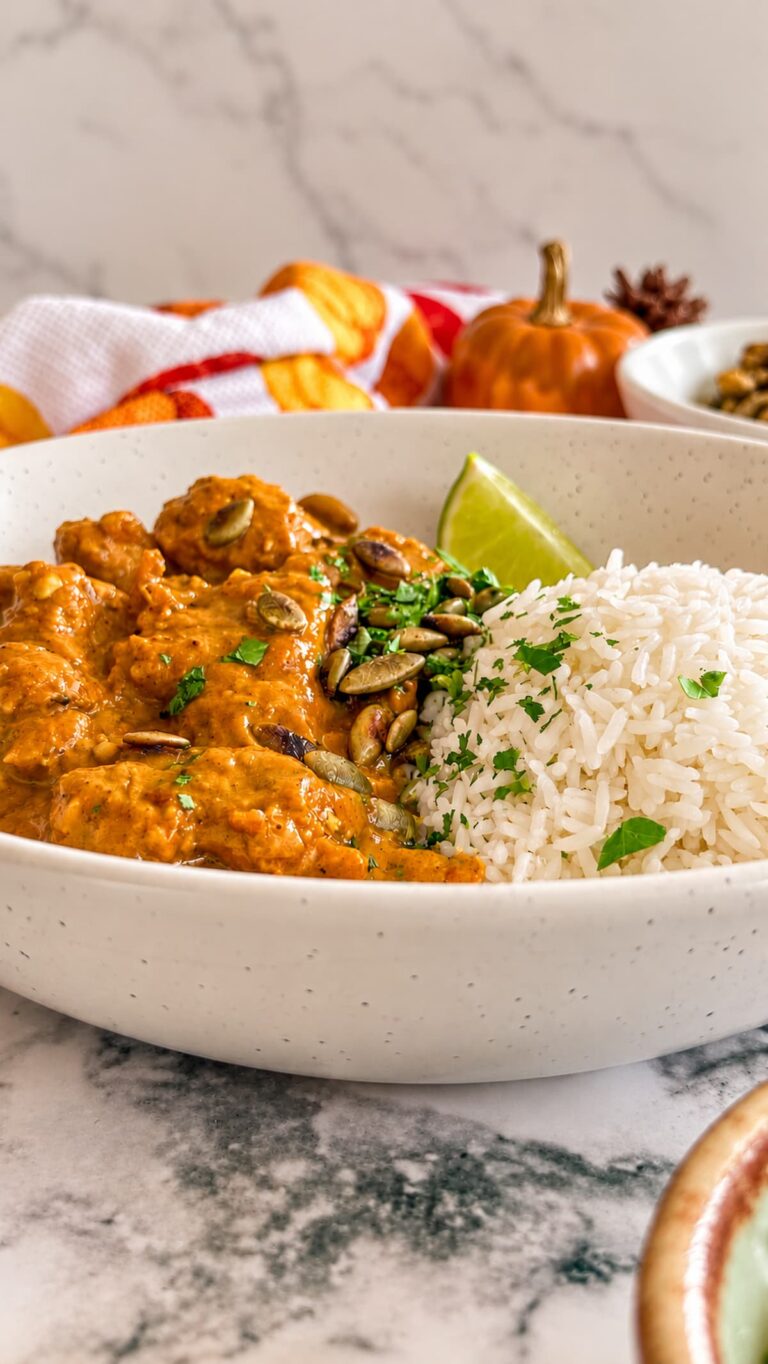 Pumpkin chicken curry with fluffy white rice, fresh cilantro, pumpkin seeds, and a lime wedge.
