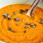 Creamy sweet potato pumpkin soup topped with pumpkin seeds and fresh sage.