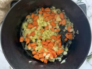 chopped onions and carrots cooking in a black dutch oven pot.