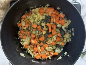 chopped carrots, onions, and garlic cooking with herbs in a pot.