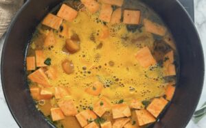 chunks of sweet potato in broth with herbs and other ingredients cooking in a pot.