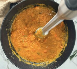 immersion blender in a pot of half blended pumpkin and sweet potato soup.