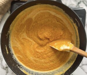 pumpkin and sweet potato soup with swirls of cream in a pot with a rubber spatula.