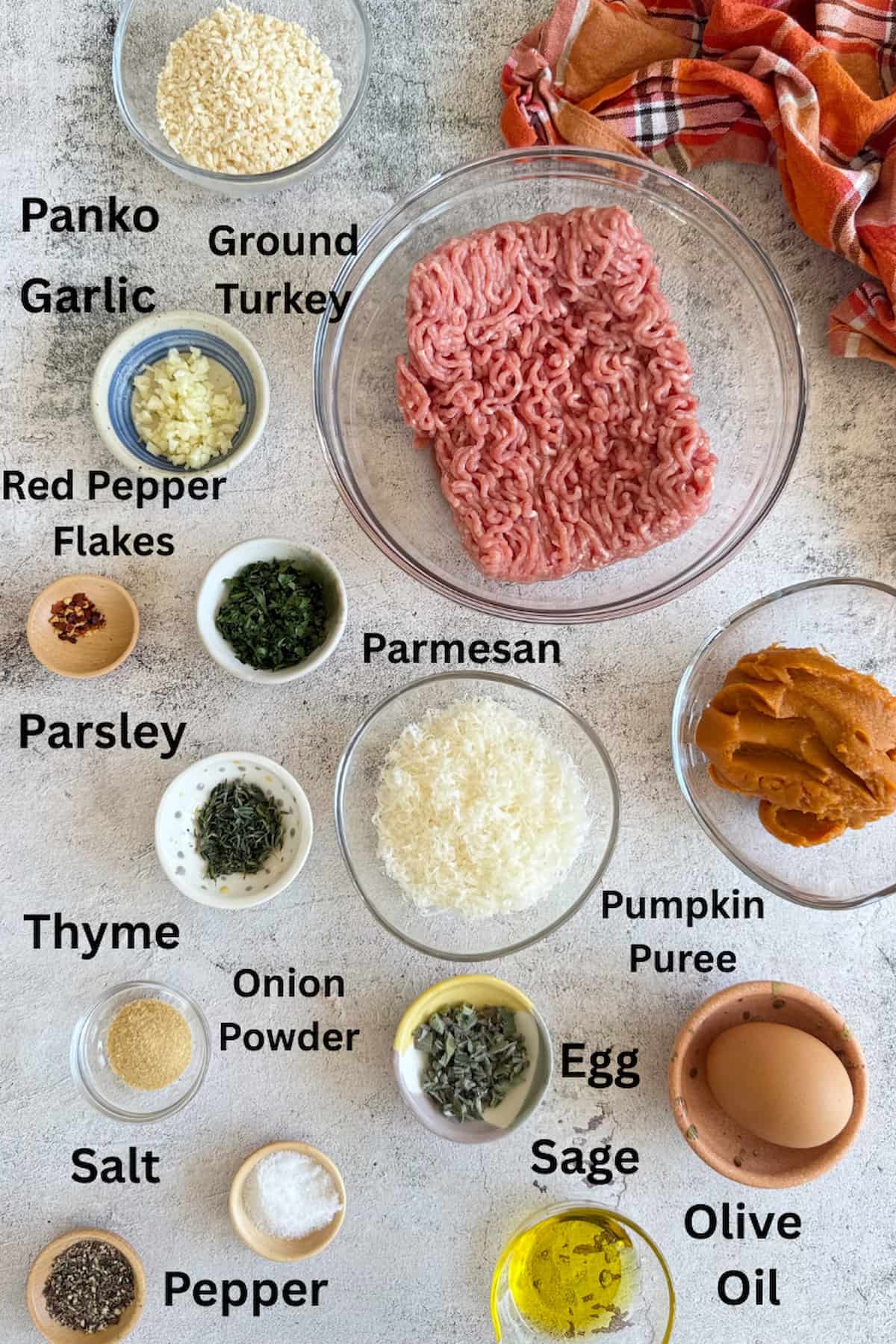 ingredients for pumpkin meatballs laid out in separate bowls - panko, garlic, ground turkey, red pepper flakes, parsley, sage, thyme, parmesan, pumpkin puree, egg, olive oil, salt, pepper, and onion powder.