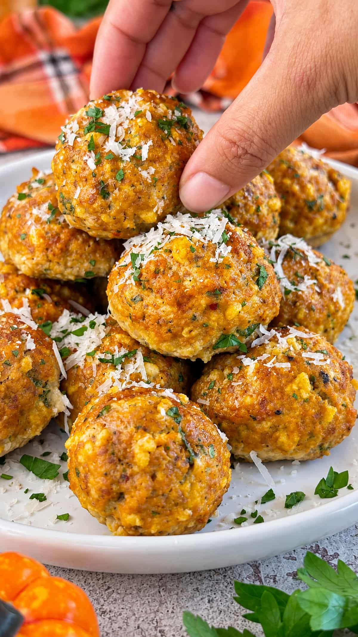 Hand grabbing a pumpkin meatball topped with grated Parmesan and fresh parsley from a serving plate.