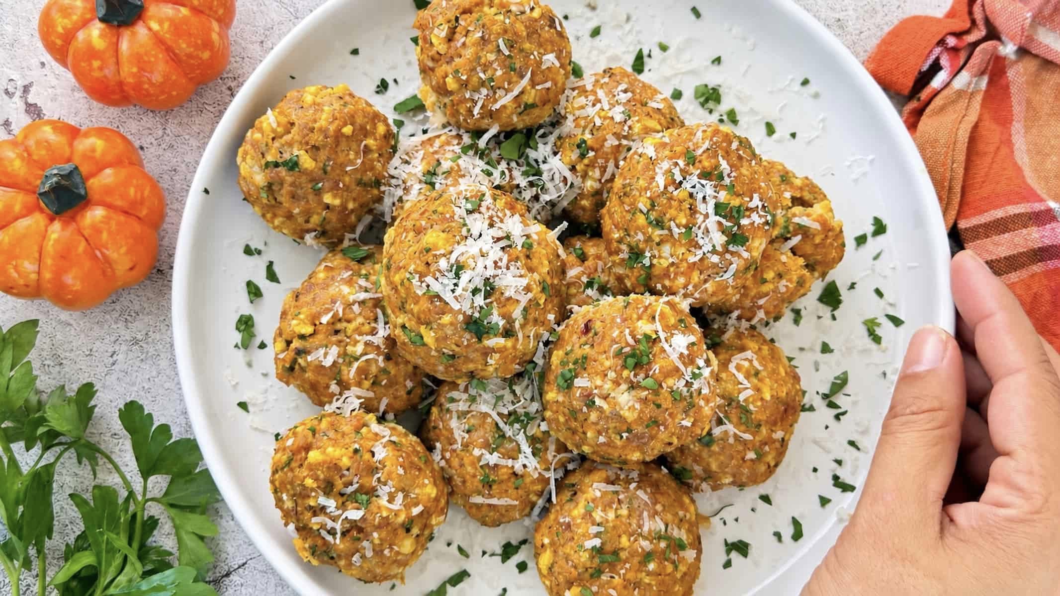 Overhead view of pumpkin meatballs topped with grated Parmesan and fresh parsley on a white serving plate.