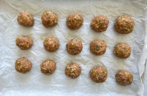 15 raw turkey pumpkin meatballs on a piece of parchment paper.