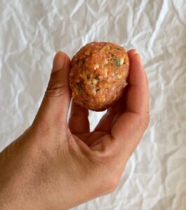 hand holding a raw pumpkin meatball over a piece of parchment paper.