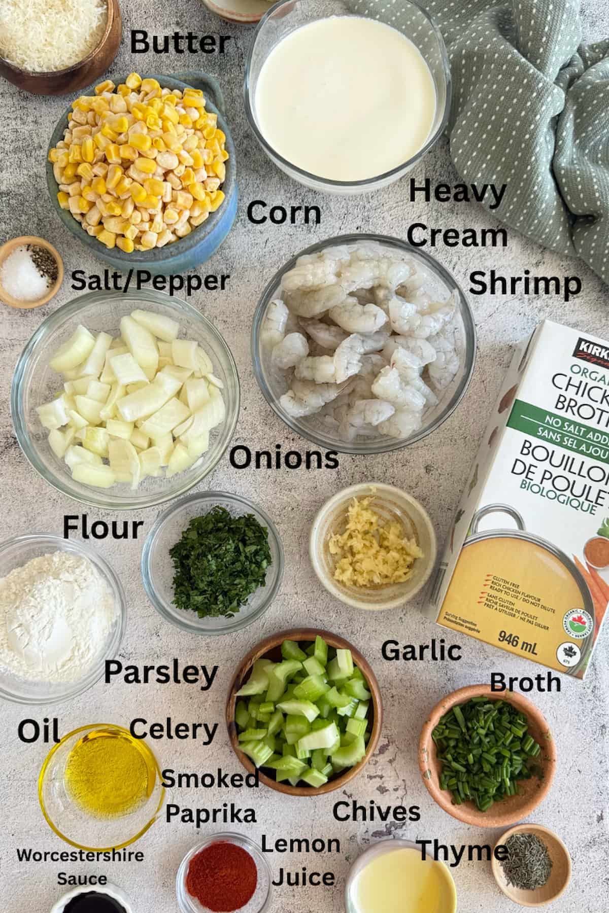 ingredients for shrimp and corn bisque laid out in separate bowls - butter, corn, salt, pepper, heavy cream, shrimp, onions, flour, garlic, broth, oil, smoked paprika, parsley, celery, chives, thyme, lemon juice, and Worcestershire sauce.