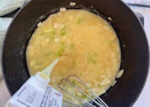 chicken broth being poured into a pot of chunky bisque with diced celery and onion.