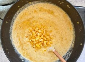 corn kernels on top shrimp and corn bisque in a black pot.