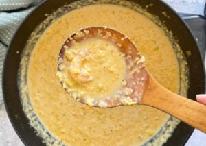 wooden spoon with a piece of shrimp over a pot of shrimp and corn bisque.