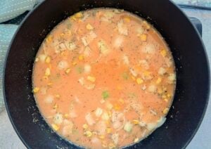 shrimp and corn bisque cooking in a large black dutch oven pot.