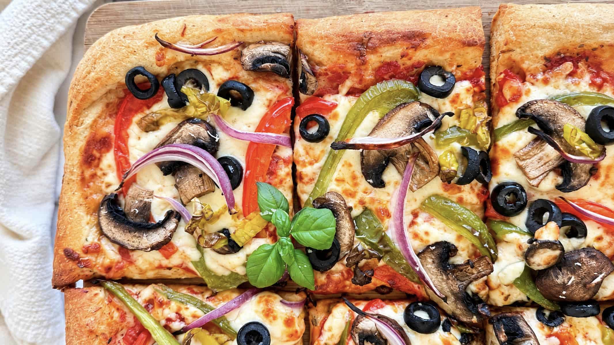Veggie delight pizza with mushrooms, bell peppers, red onion, black olives, melted cheese, and fresh basil.