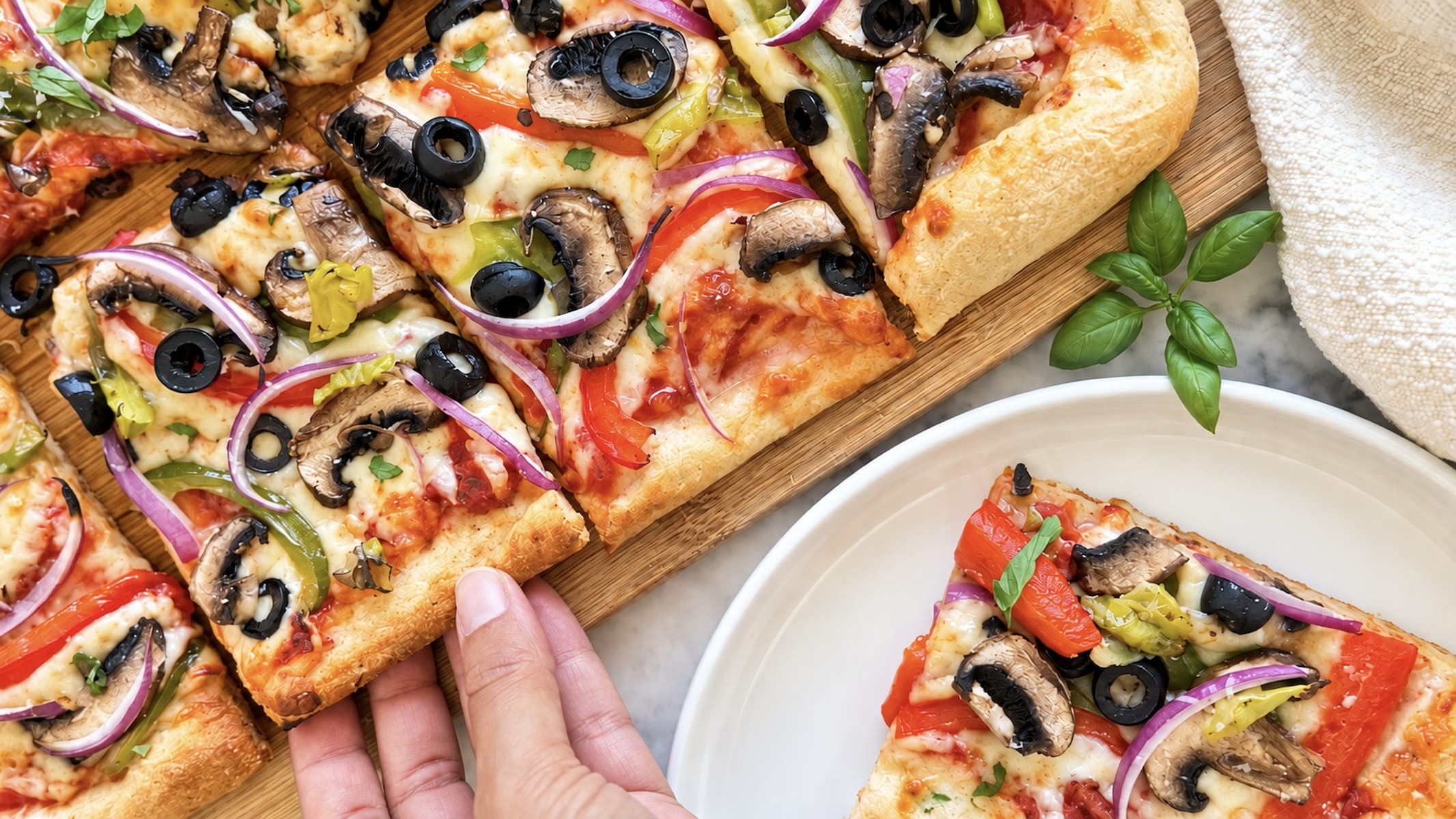Veggie delight pizza topped with mushrooms, bell peppers, red onion, black olives, melted cheese, and fresh basil.