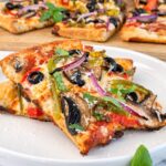 Veggie delight pizza slices topped with mushrooms, bell peppers, red onion, black olives, melted cheese, and fresh basil.