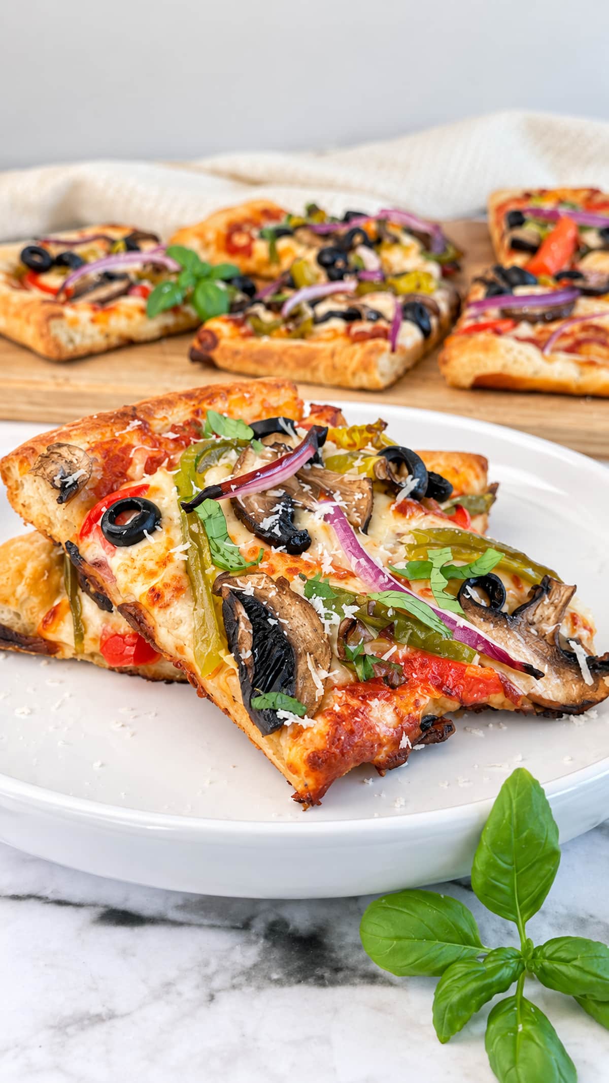 Veggie delight pizza slices topped with mushrooms, bell peppers, red onion, black olives, melted cheese, and fresh basil.
