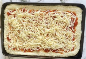 unbaked cheese pizza on a baking sheet.