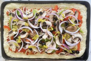 unbaked veggie supreme pizza with black olives, red onions, pepperoncini, bell peppers, mushrooms, mozzarella, and pizza sauce.