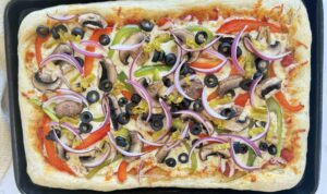 baked veggie supreme pizza with black olives, red onions, pepperoncini, bell peppers, mushrooms, mozzarella, and pizza sauce.
